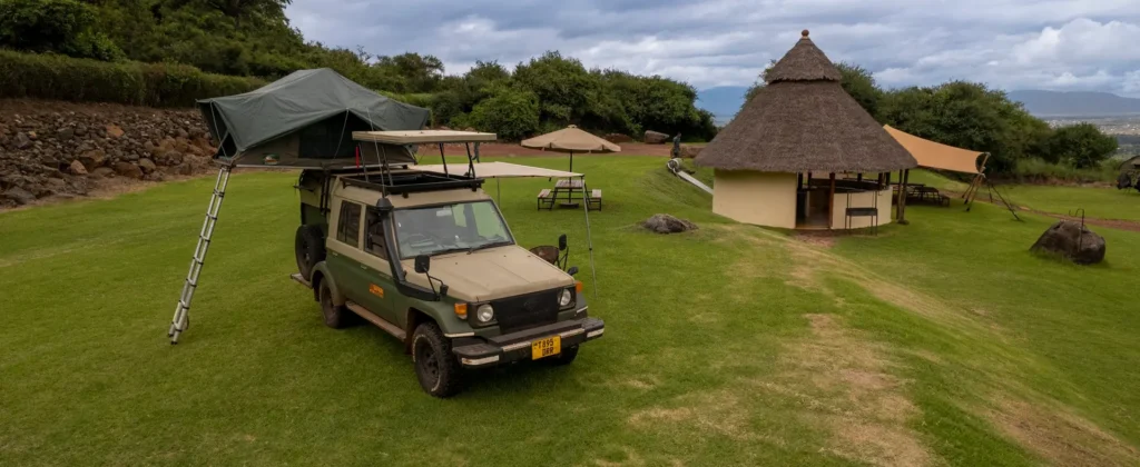 A jeep with a tent mounted on its roof, situated in a grassy area, showcasing adventure and Tanzania safety.