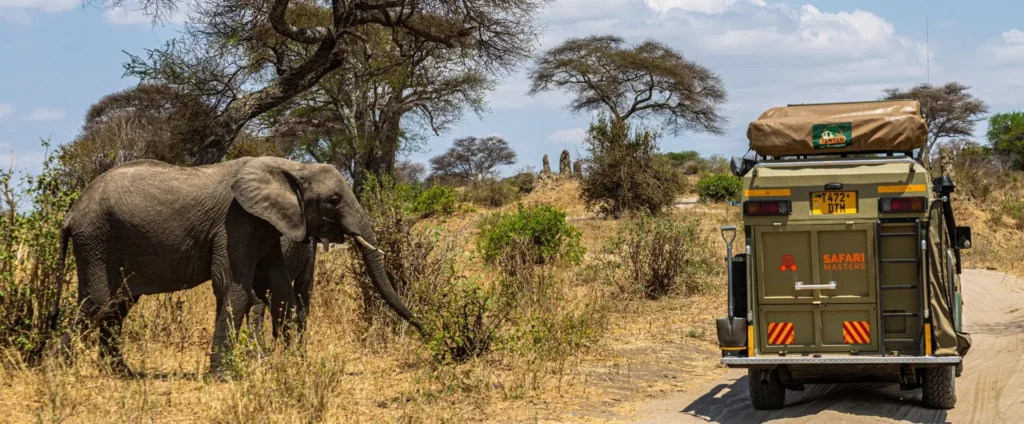 A truck with a tent on top drives along a dirt road, showcasing the best time to visit Tanzania scenic landscapes.
