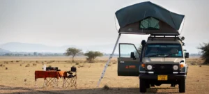 A vehicle equipped with a rooftop tent stands in a field, representing a camping in Tanzania experience.