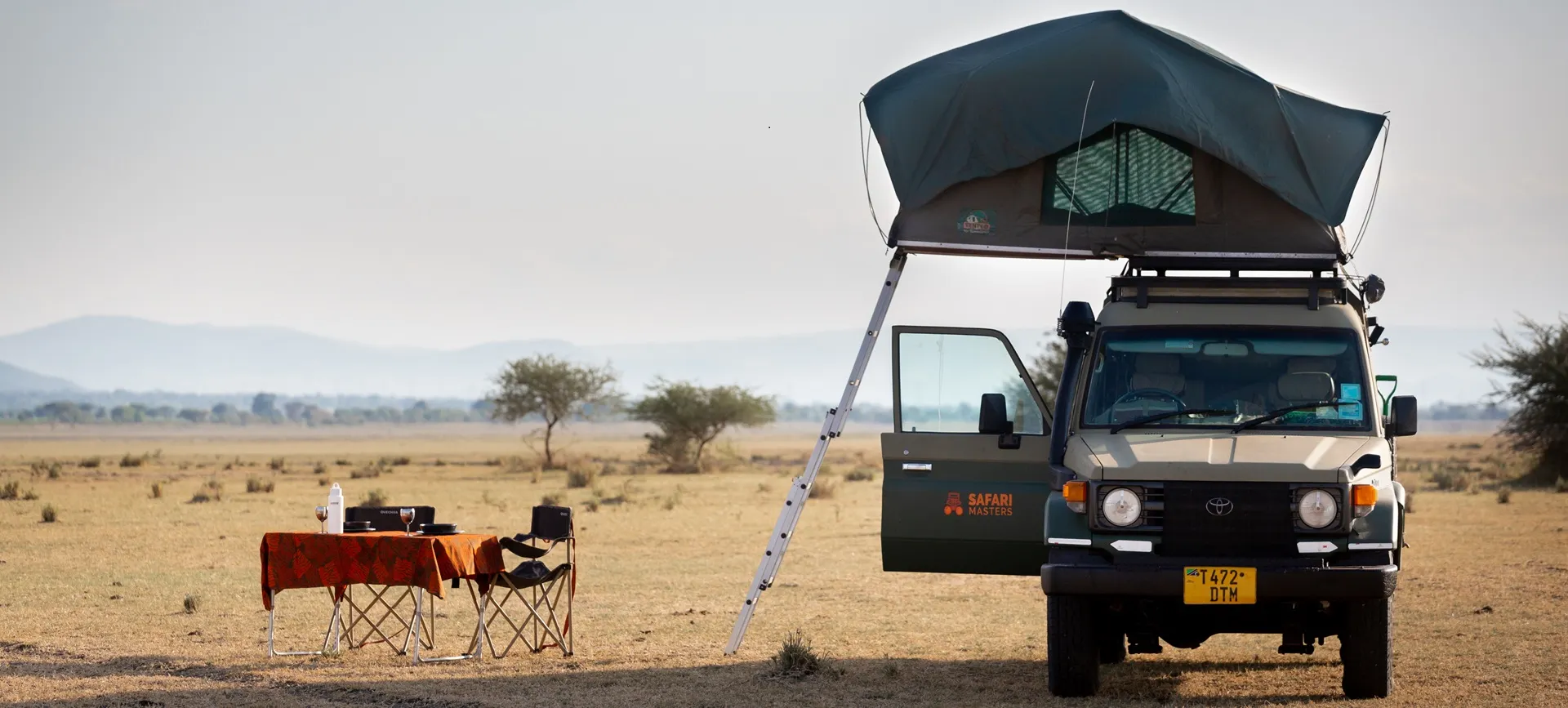 Un vehículo equipado con una tienda de techo está en un campo, representando una experiencia de acampada en Tanzania.