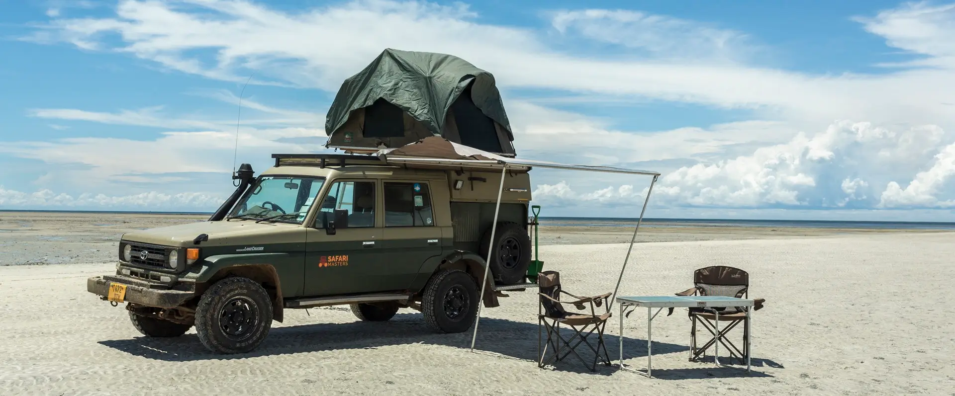 Un todoterreno con una tienda en el techo, estacionado en la playa, que representa la esencia de un viaje sobre el coste de safari en Tanzania.