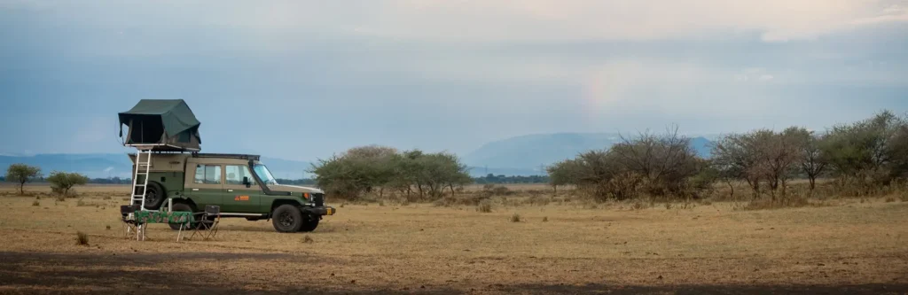 A jeep with a tent on top parked in a field, showcasing a camping in Kenya adventure in the great outdoors.