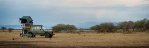 A jeep with a tent on top parked in a field, showcasing a camping in Kenya adventure in the great outdoors.