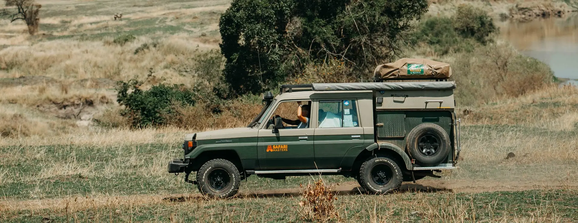 Un jeep verde circula por la hierba exuberante, destacando a un guía conductor en Kenia en un viaje de aventura.