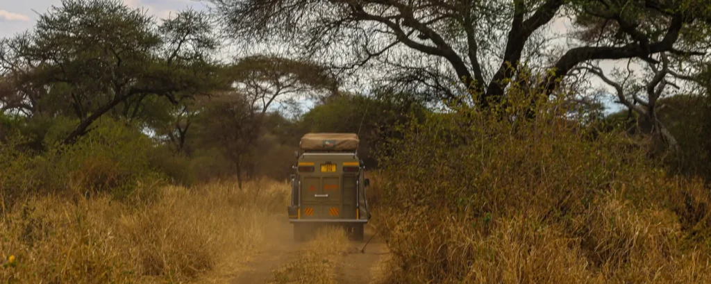 A Safari Masters 4x4 Vehicle navigates a dirt road surrounded by trees in Kenya, illustrating the experience of driving in Kenya.