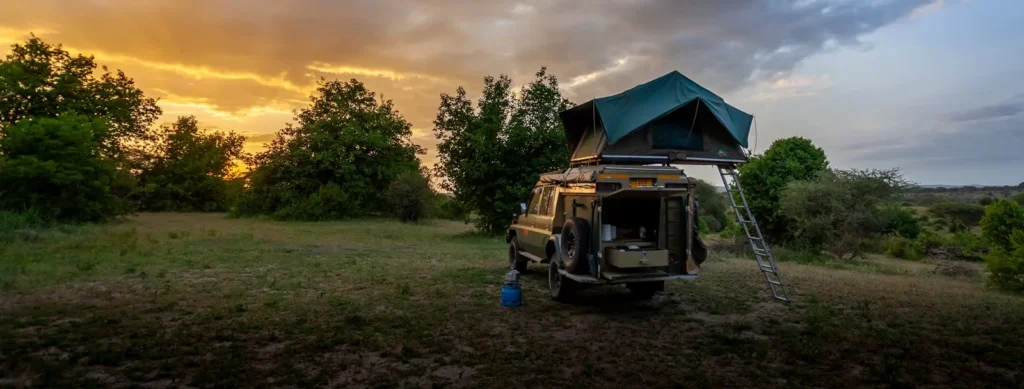 A camper van with a tent on top, silhouetted against a vibrant sunset, showcasing the best time to visit Uganda.