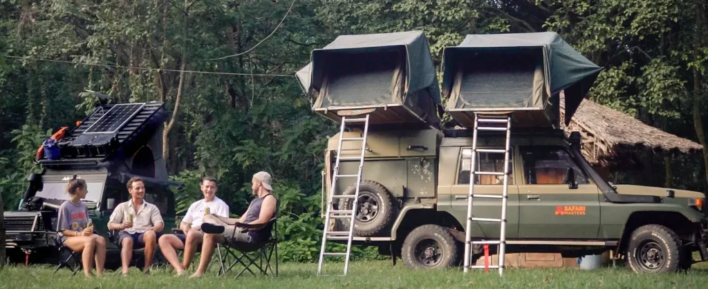 A group of people sitting on chairs near a vehicle, enjoying a camping in Uganda experience.