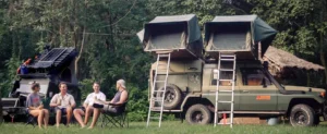 A group of people sitting on chairs near a vehicle, enjoying a camping in Uganda experience.