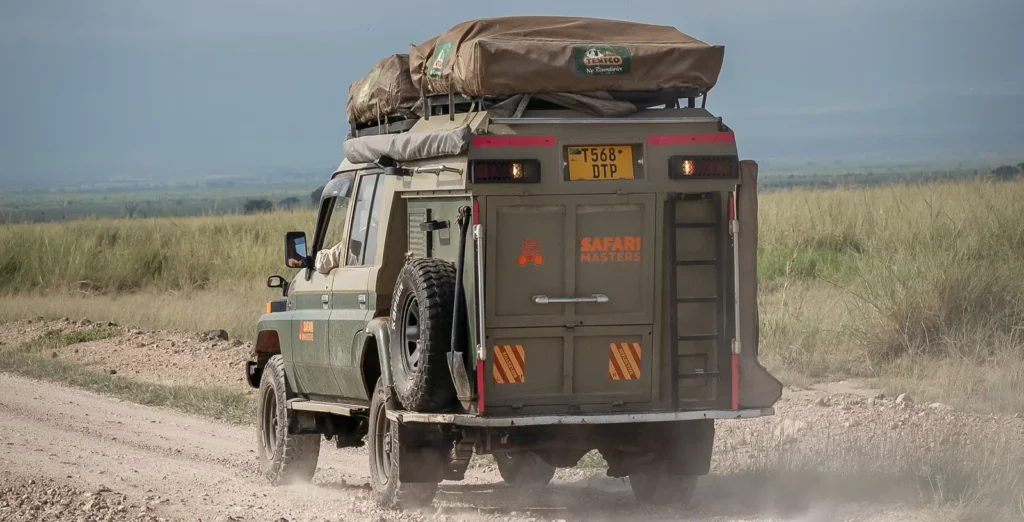 A vehicle drives on a dirt road with a tent on top, illustrating adventure amidst uganda entry requirements.