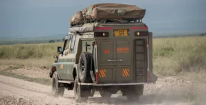 A vehicle drives on a dirt road with a tent on top, illustrating adventure amidst uganda entry requirements.