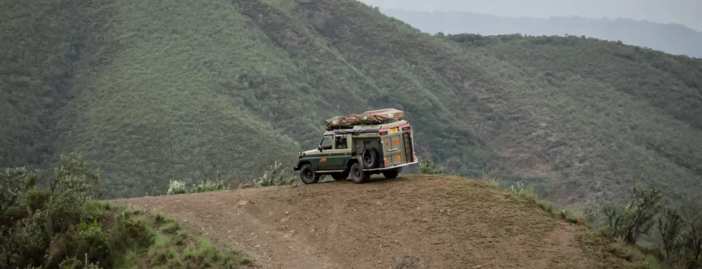 A truck loaded with luggage travels down a dirt road, emphasizing uganda national parks fees and permits for visitors.