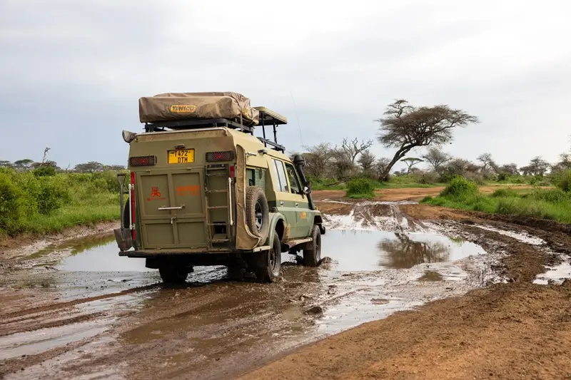 A vehicle driving through a muddy road, showcasing the conditions in the Masai Mara, where entry fees are required.