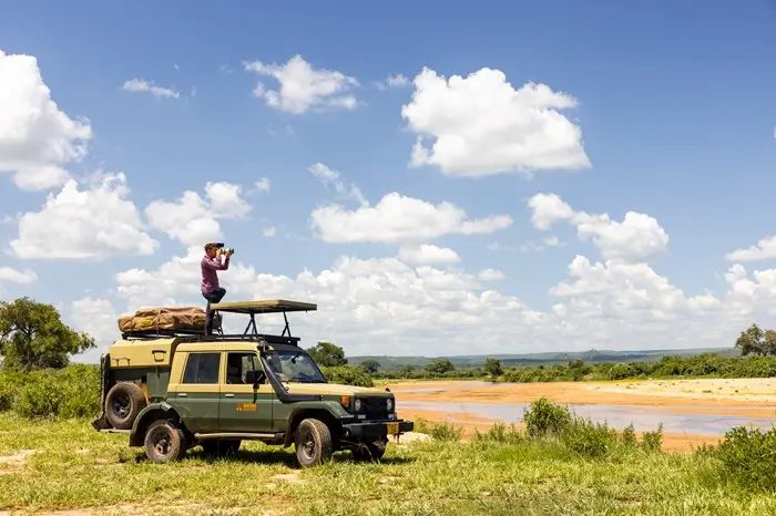 A woman stands on a vehicle in the wild Serengeti, emphasizing the beauty of nature and the relevance of Serengeti National Park fees.